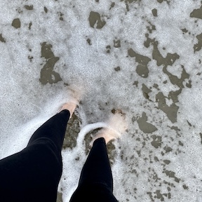 A pair of feet on the beach being gently kissed by the Pacific ocean.